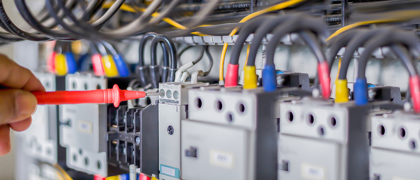 Professional electrician testing commercial electrical panel with multimeter red probe on circuit breakers with color coded wiring for business electrical services