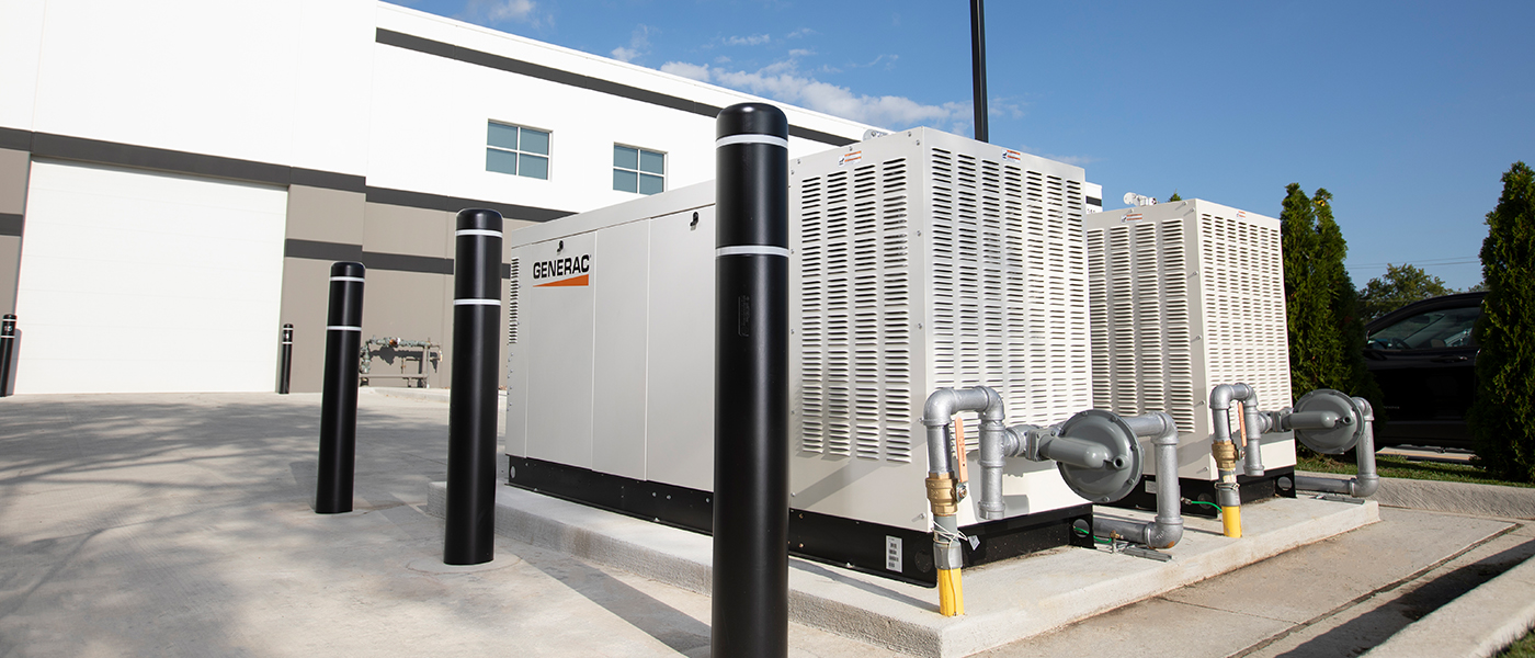 Industrial Generac standby generator with protective bollards installed outside commercial building, providing backup power for business operations