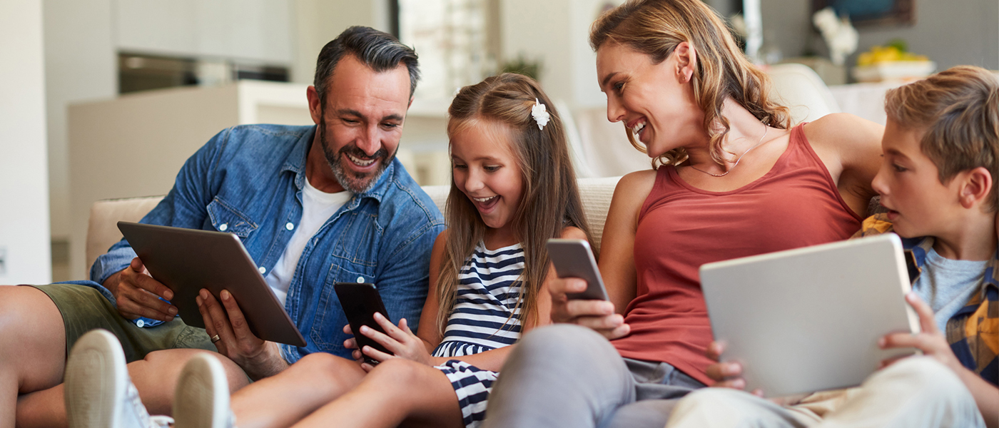Happy family of four using multiple devices on couch tablets phones and laptop wireless internet installation services for residential homes