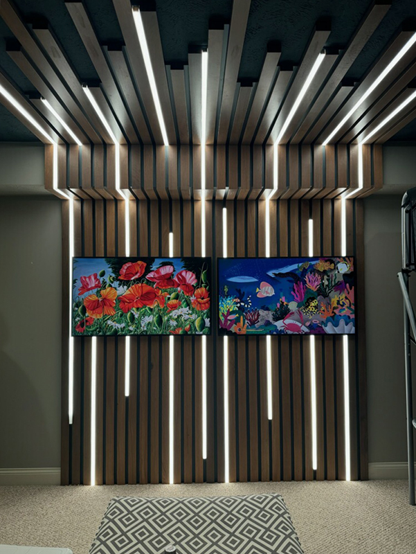 Two wall-mounted display screens showing colorful floral and underwater imagery on decorative slatted wooden wall with integrated LED lighting strips in contemporary home theater or entertainment space